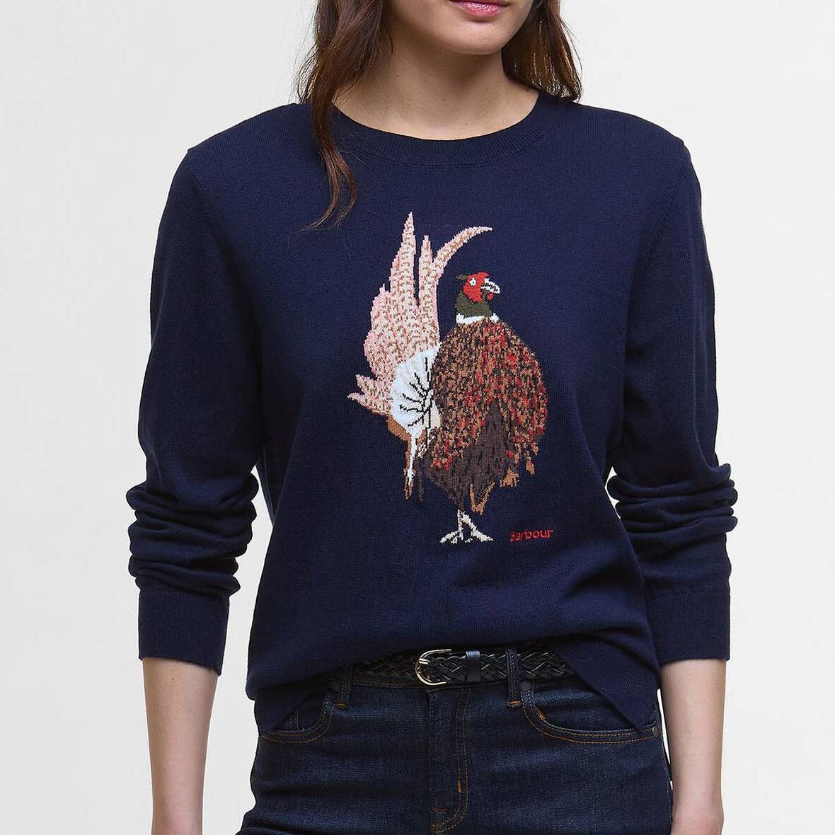 Woman wearing a navy Barbour sweater with a pheasant design on a light gray background